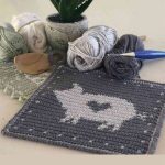 Crochet Pig Hot Pad. White pig on grey background, with yarn and crochet hook at the side || thecrochetspace.com