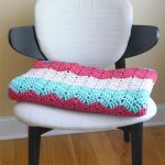 Crocheted Boardwalk Breeze Blanket. Folded blanket on chair, crafted in pink, turquoise and white || thecrochetspace.com
