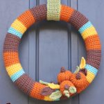 Delightful Crocheted Fall Wreath. Crafted in harvest colors and blue stripes with pumpkin accents. Image of wreath on door || thecrochetspace.com