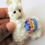 Larry Llama Crochet Brooch. Llarma being held. With brightly colcored blanket over back || thecrochetspace.com