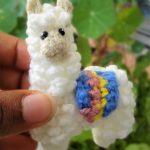 Larry Llama Crochet Brooch. Held between fingers. Fluffy white with bright blanket || thecrochetspace.com