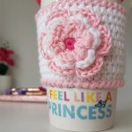 Mug Hugger Crocheted Coffee Cozy. Mug cozy in white with pink edging with accent flower in same pink and white added || thecrochetspace.com