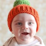 Pumpkin Parker Crocheted Hat. Front image of little tot wearing an orange beanie with green bobble || thecrochetspace.com