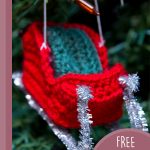 Santa's Festive Crochet Sleigh. Red sleith with green seating and silver running blades hanging in a christmas tree || thecrochetspace.com