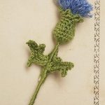 Scottish Thistle Crochet Flora. Blue head and two green leaves, placed at an angle on beige card || thecrochetspace.com
